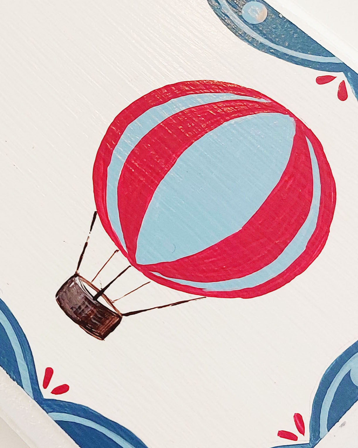 Close-up view of a personalized nursery door sign featuring a red and blue hot air balloon, part of a customizable baby room decor with a blue scalloped edge design.
