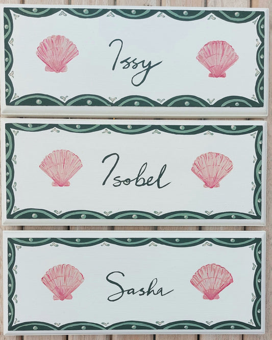 Nursery door sign personalised with the names 'Issy', 'Isobel' and 'Sasha', featuring whimsicle sea shells and a decorative blue scalloped border, perfect for baby room decor.