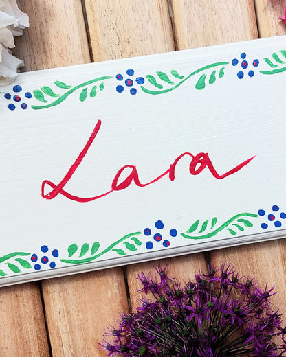 Nursery door sign personalised with the name 'Lara', featuring striking grenadier guards and a decorative blue and green floral border, perfect for baby room decor.