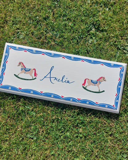 Nursery door sign personalised with the name 'Amelia', featuring beautiful rocking horses and a decorative blue scalloped border, perfect for baby room decor.