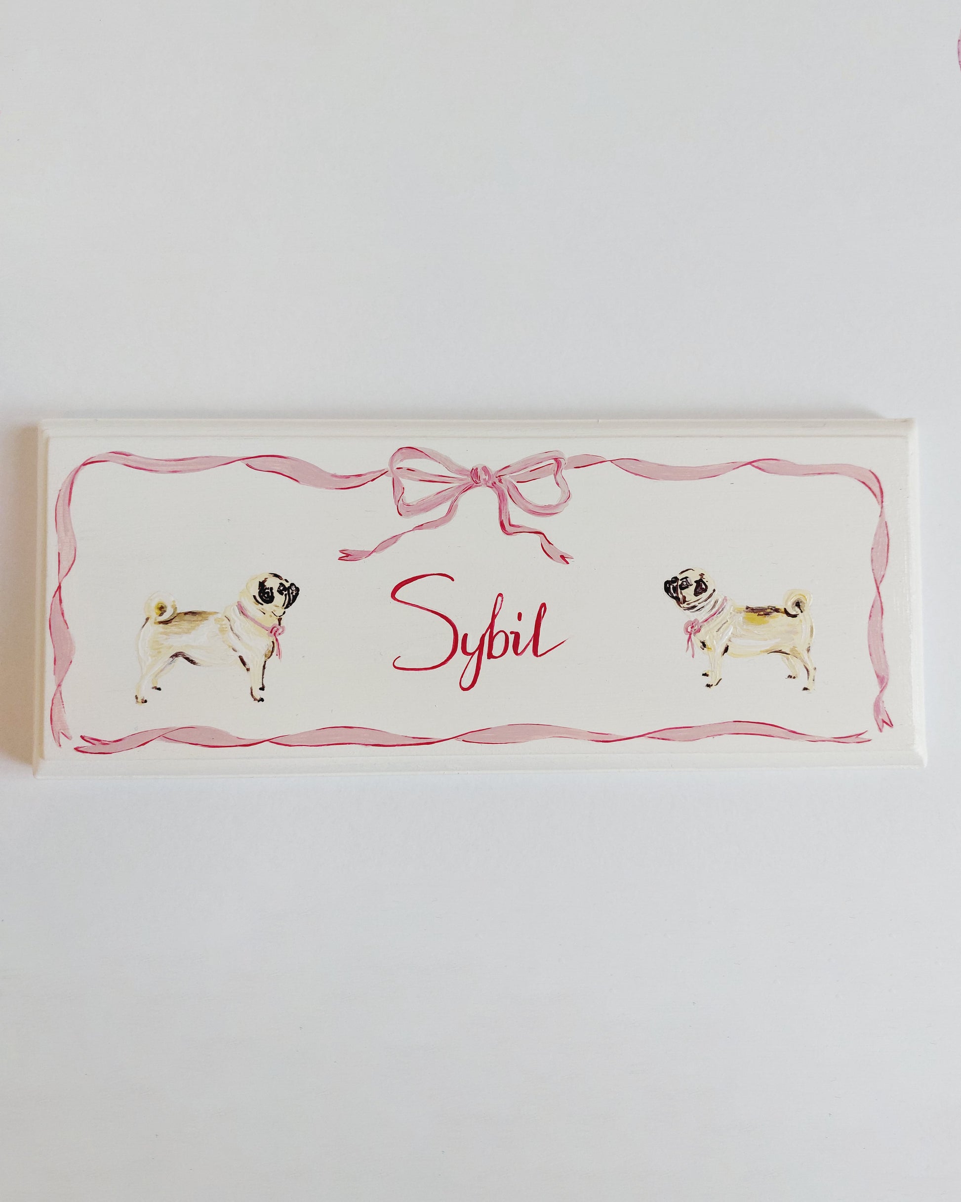 Nursery door sign personalised with the name 'Sybil', featuring adorable dogs and a decorative pink bow and ribbon border, perfect for baby room decor.