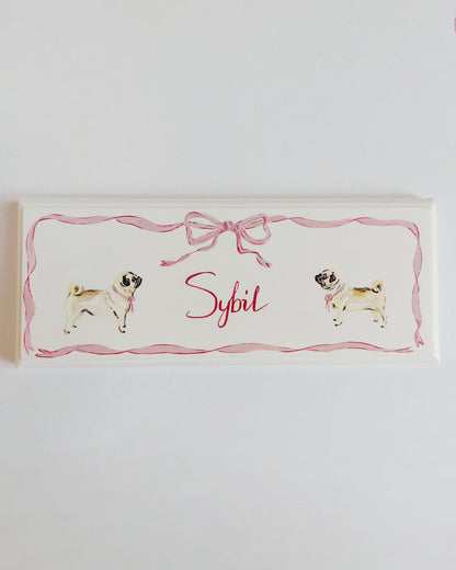 Nursery door sign personalised with the name 'Sybil', featuring adorable dogs and a decorative pink bow and ribbon border, perfect for baby room decor.