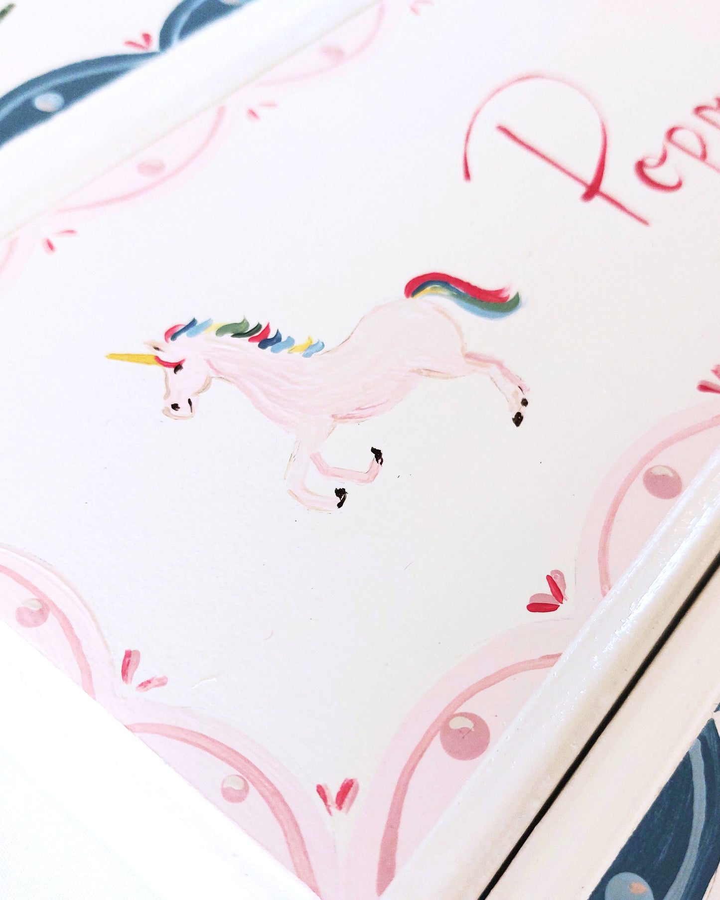 A close-up of a nursery door sign personalised with the name 'Poppy', featuring magical rainbow-maned unicorns and a decorative pink scalloped border, perfect for baby room decor.