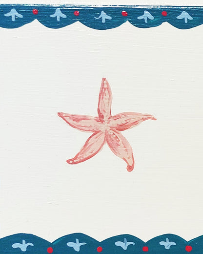 Close up of a nursery door sign personalised with the name 'Nancy', featuring whimsible starfish and a decorative blue scalloped border, perfect for baby room decor.