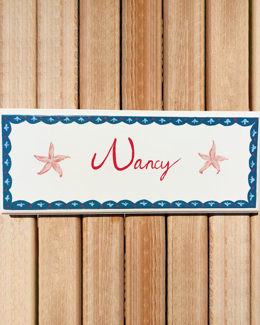 Nursery door sign personalised with the name 'Nancy', featuring whimsible starfish and a decorative blue scalloped border, perfect for baby room decor.