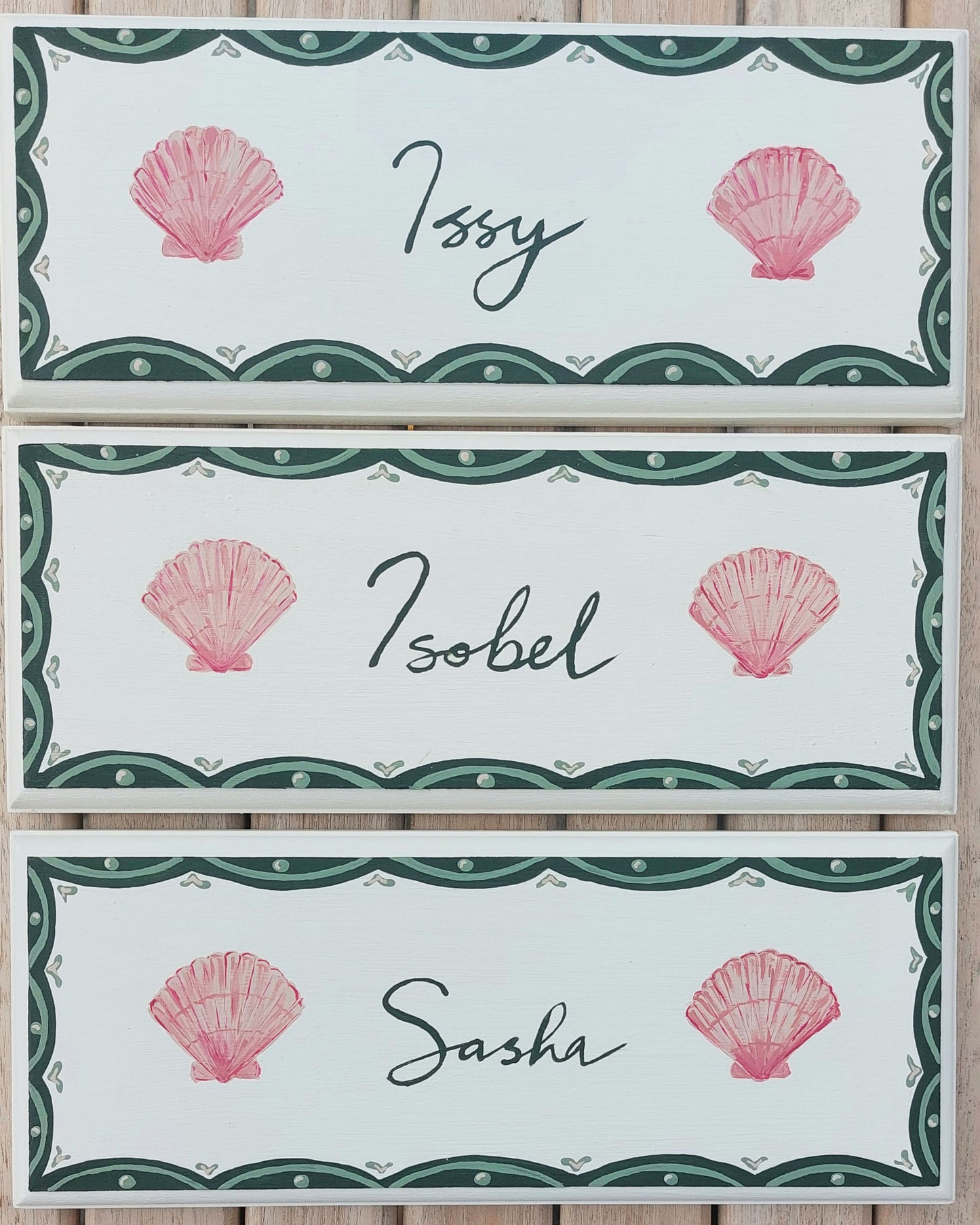 Nursery door sign personalised with the names 'Issy', 'Isobel' and 'Sasha', featuring whimsicle sea shells and a decorative blue scalloped border, perfect for baby room decor.