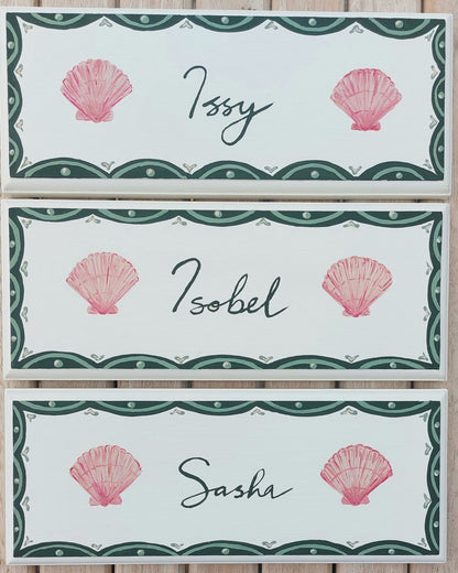 Nursery door sign personalised with the names 'Issy', 'Isobel' and 'Sasha', featuring whimsicle sea shells and a decorative blue scalloped border, perfect for baby room decor.