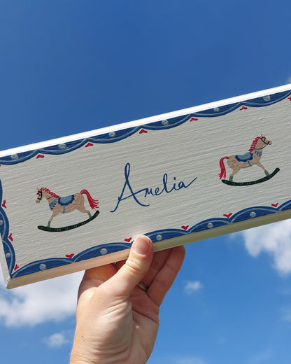 Nursery door sign personalised with the name 'Amelia', featuring beautiful rocking horses and a decorative blue scalloped border, perfect for baby room decor.