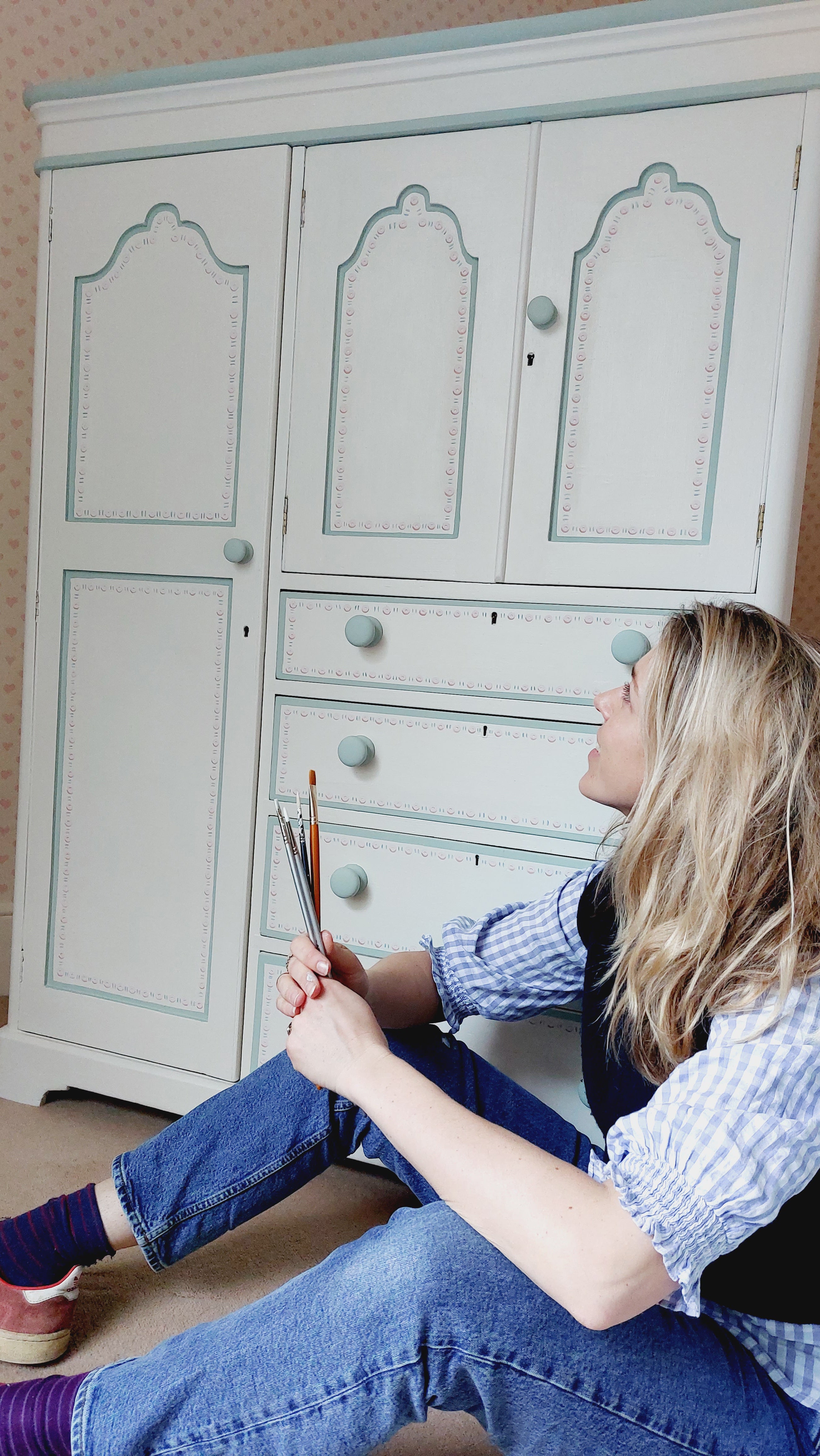 Artist Emma shown sitting with a large dresser she has designed for a customer