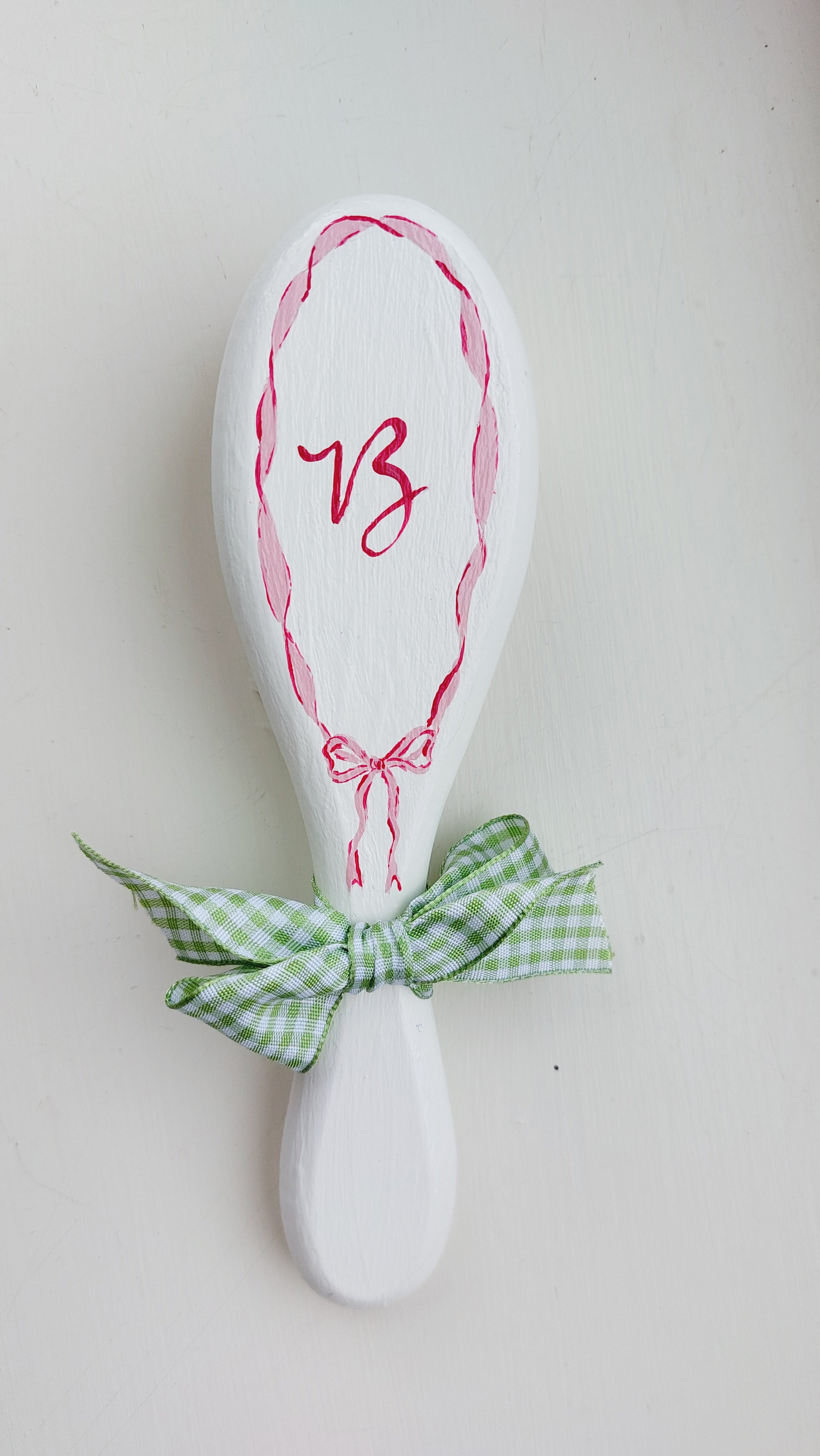 A hand painted custom hair brish with a gingham ribbon on the handle and the letter 'B' on the paddle.